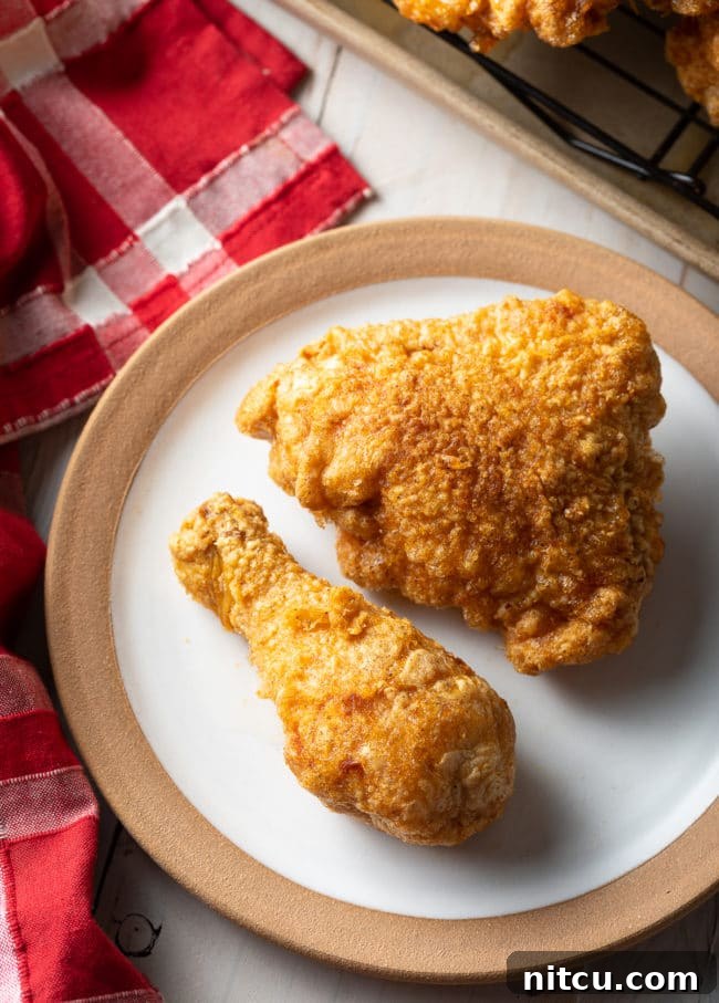 Ultimate Tavern Style Fried Chicken 10 Top-down view of a breaded fried chicken thigh and drumstick on a white plate, ready to be enjoyed.