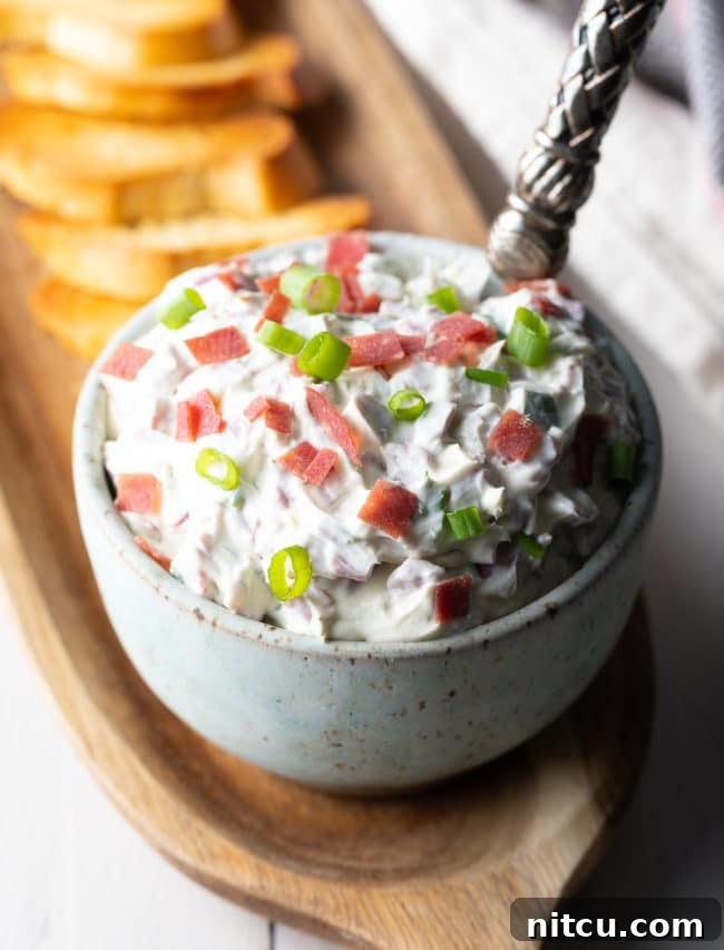 Chipped Beef Dip in a small bowl on a wooden serving platter next to toasted bread. 