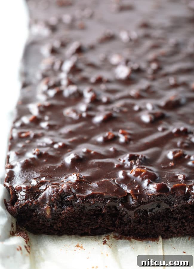 Chocolate-Sheet-Cake-Recipe Texas Sheet Cake on a pan lined with parchment paper with part of the cake cut into.