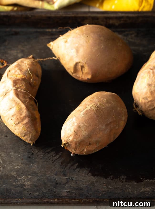 old-fashioned Baked sweet potatoes, whole and tender, arranged on a baking sheet, illustrating the initial step in preparing an old-fashioned sweet potato pie from scratch.