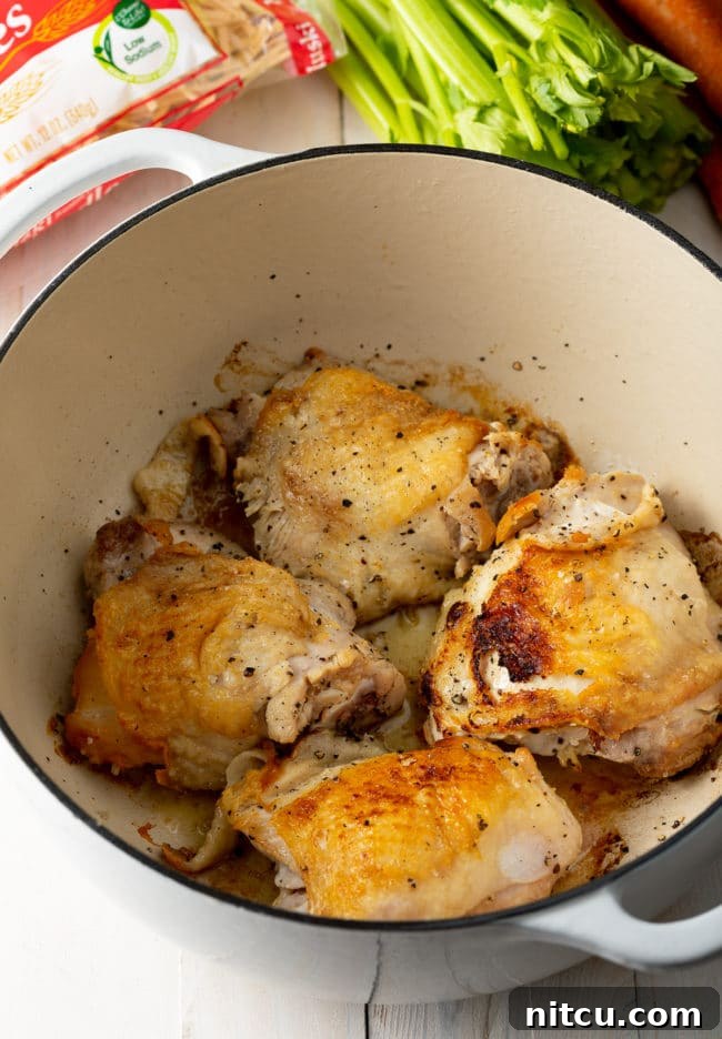 A step in the chicken noodle soup making process, showing ingredients being added to a pot.