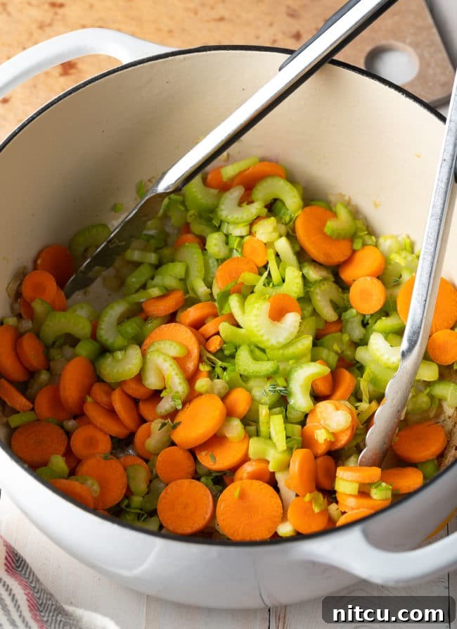 Sliced carrots and celery being sautéed in a large Dutch oven, preparing for the broth addition.