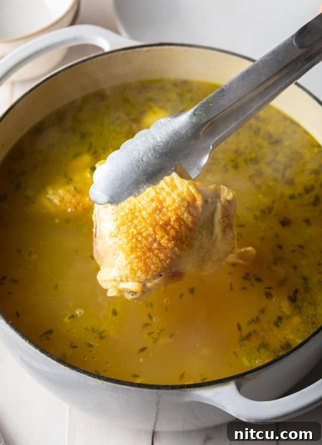 Tender chicken thighs being returned to the simmering pot of aromatic chicken noodle soup.