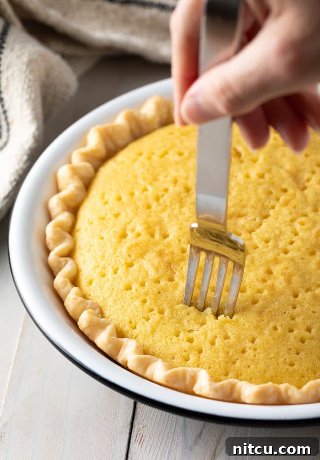 Luscious Tres Leches Pie 9 A fork pricking holes into the freshly baked sponge cake within the pie crust, preparing it to absorb the Tres Leches mixture.