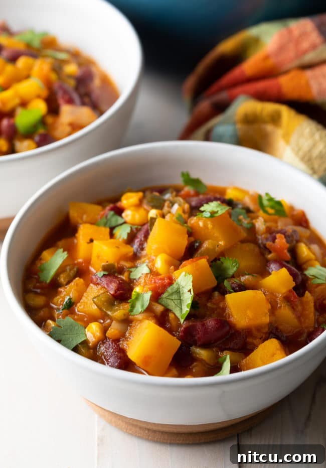 Hearty Butternut Chili 3 A steaming bowl of vegetarian chili, showcasing chunks of butternut squash, kidney beans, and corn, garnished with fresh cilantro.