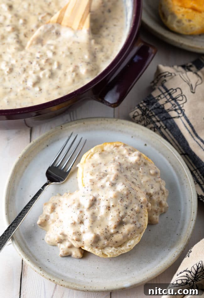 Effortless Homemade Sausage Gravy 3 Biscuit on a plate smothered in spicy sausage gravy with a fork.