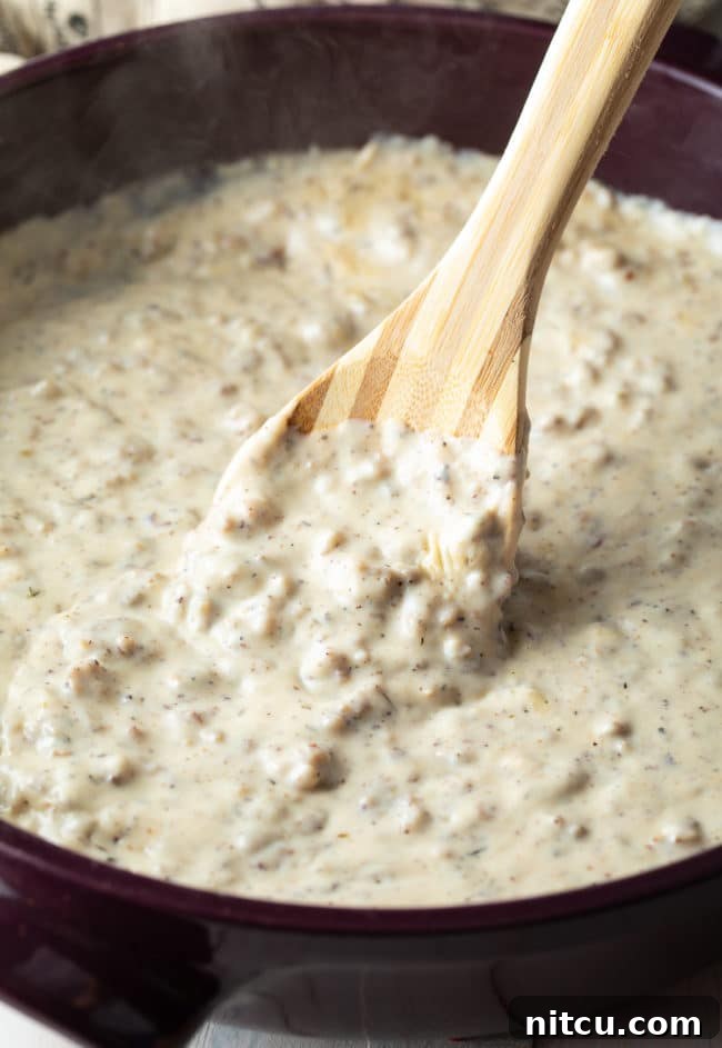 Effortless Homemade Sausage Gravy 6 Stirring Easy Sausage Gravy Recipe in a skillet with a wooden spoon.