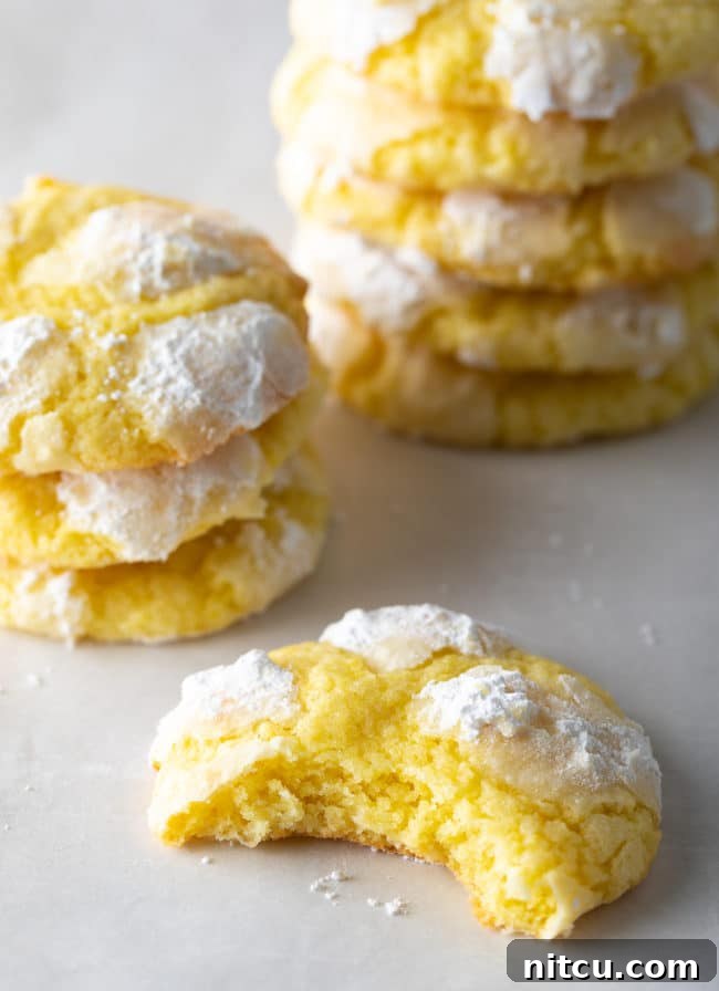 Zesty Lemon Crinkles 11 A delicious Lemon Crinkle Cookie with a bite taken out, revealing its soft interior, with more cookies stacked beautifully in the background.