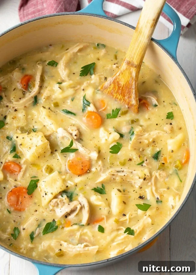 A large Dutch oven filled with creamy, rich chicken and dumplings, with a wooden spoon resting in the pot. The dish is steaming, highlighting its warmth and comforting nature.