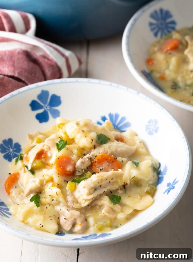 A close-up shot of a bowl overflowing with thick, creamy chicken and dumplings, garnished with fresh black pepper and parsley.