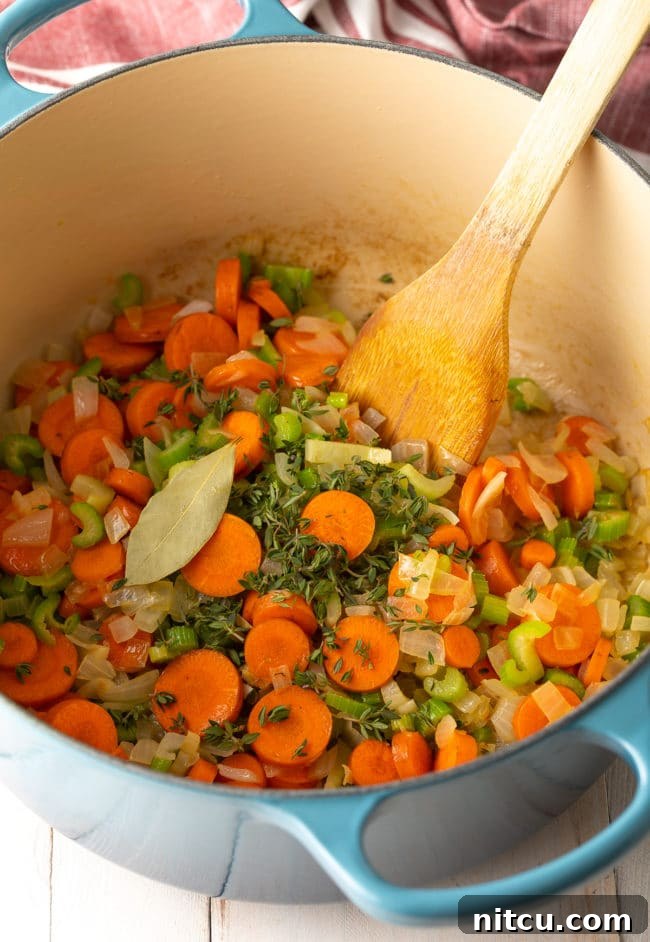 Freshly chopped onions, celery, and carrots are being sautéed in melted butter in a large soup pot, releasing aromatic steam.