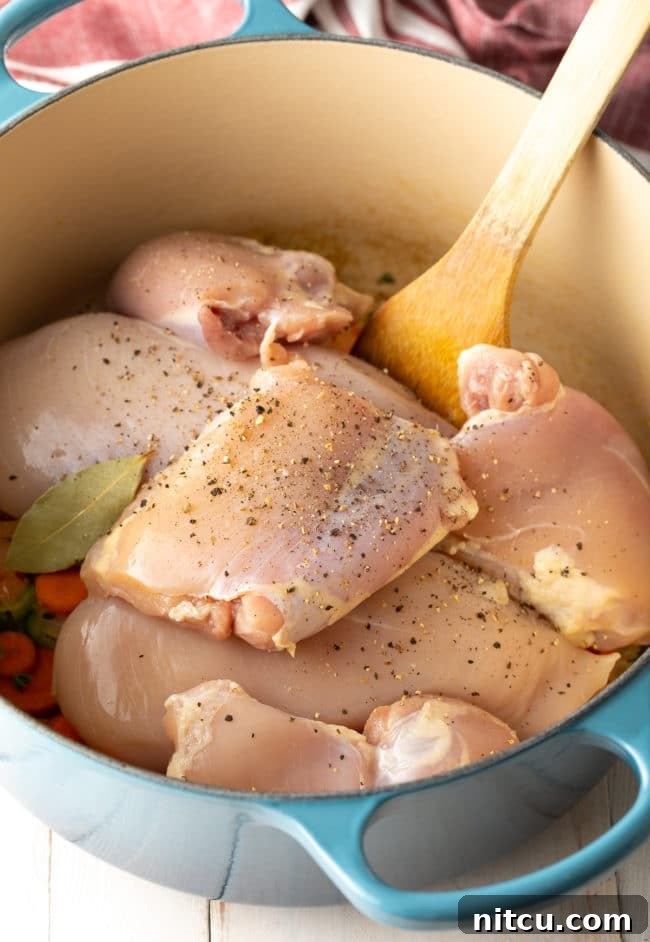 Raw boneless chicken pieces are added to a pot with sautéed vegetables and broth, ready for simmering to create the soup base for chicken and dumplings.