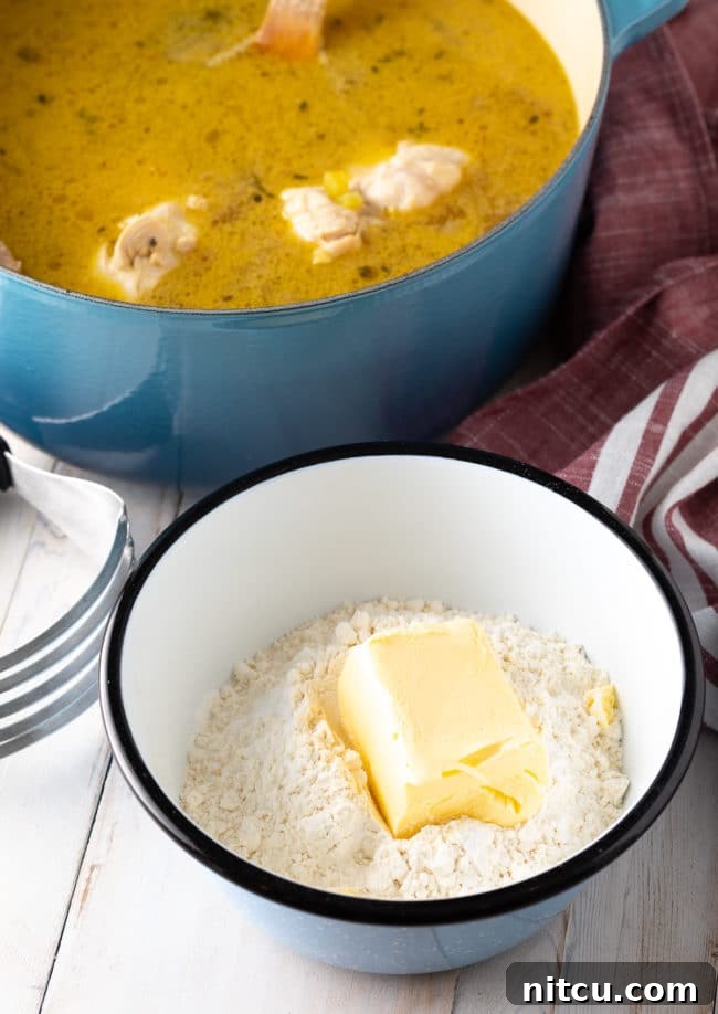 A bowl containing all-purpose flour and cubes of butter-flavored vegetable shortening, positioned next to a blue Dutch oven, ready for dumpling preparation.