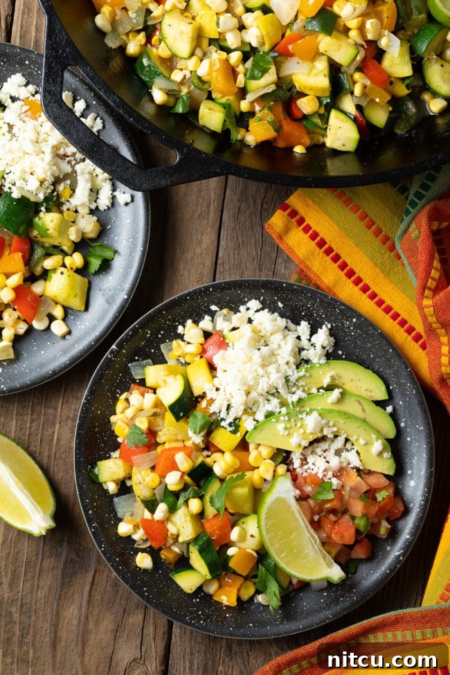 Calabacitas Con Queso Recipe - Sauteed squash, zucchini and corn served on a plate with cheese, avocado and lime, ready to be enjoyed.
