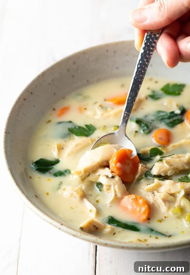 A spoon scooping up a delicious bite of creamy lemon chicken soup from a rustic bowl.