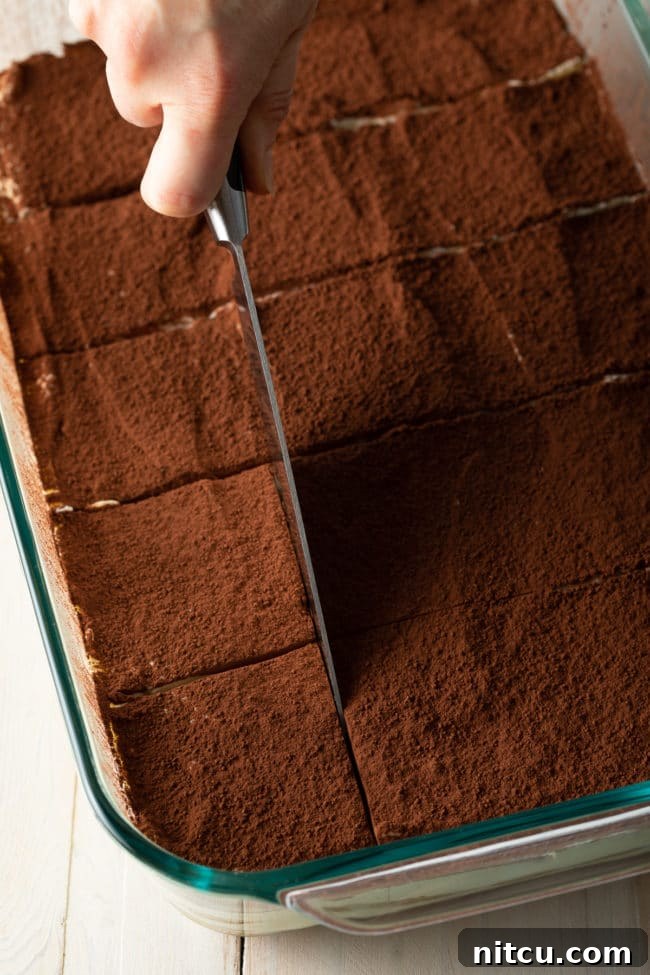Espresso Pick-Me-Up Delight 12 A hand holding a sharp knife, carefully slicing the easy tiramisu into neat squares, ready for serving.