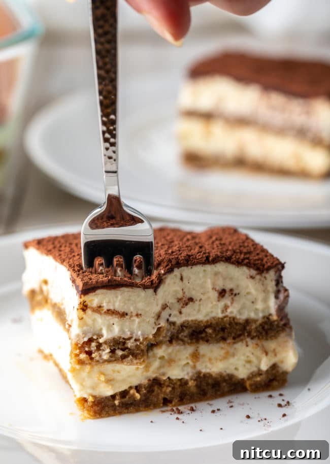 Espresso Pick-Me-Up Delight 16 Easy Tiramisu Recipe - a beautiful slice on a plate with a fork gently breaking into the creamy layers.
