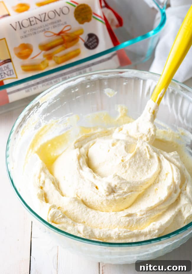 Espresso Pick-Me-Up Delight 8 A rubber spatula gently folding mascarpone and whipped heavy cream together in a glass bowl, ensuring a light and airy texture for the tiramisu filling.