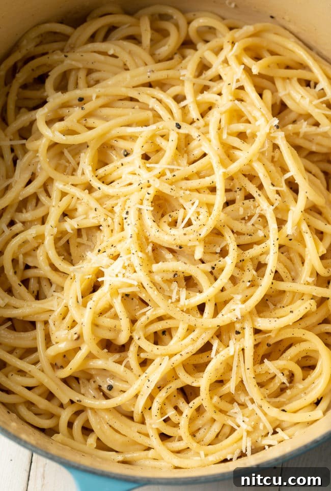Cacio e Pepe cooking in a large blue pot, showing the pasta submerged in broth.