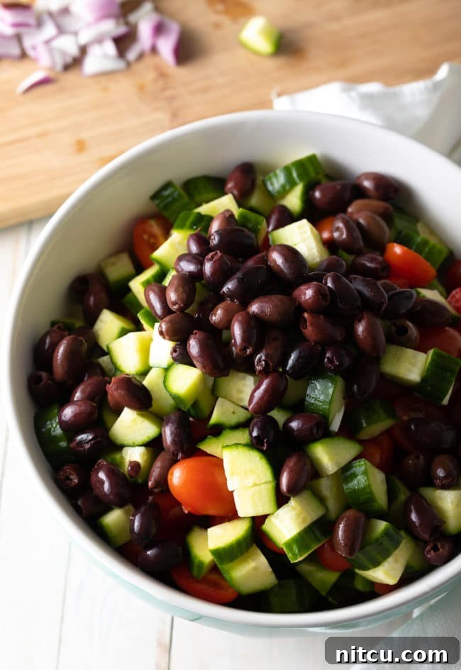 Meal Prep: Greek Pasta Salad Recipe. A container of pasta salad with ingredients ready for a healthy vegetarian meal.