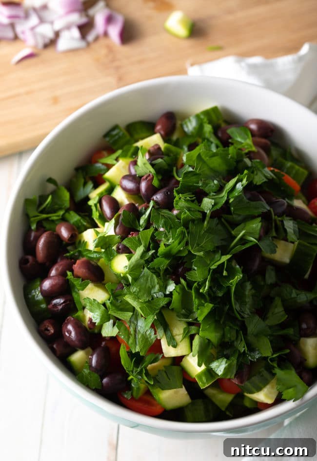 Individual ingredients for Greek Pasta Salad, including pasta, fresh vegetables, olives, and feta cheese, in separate bowls.