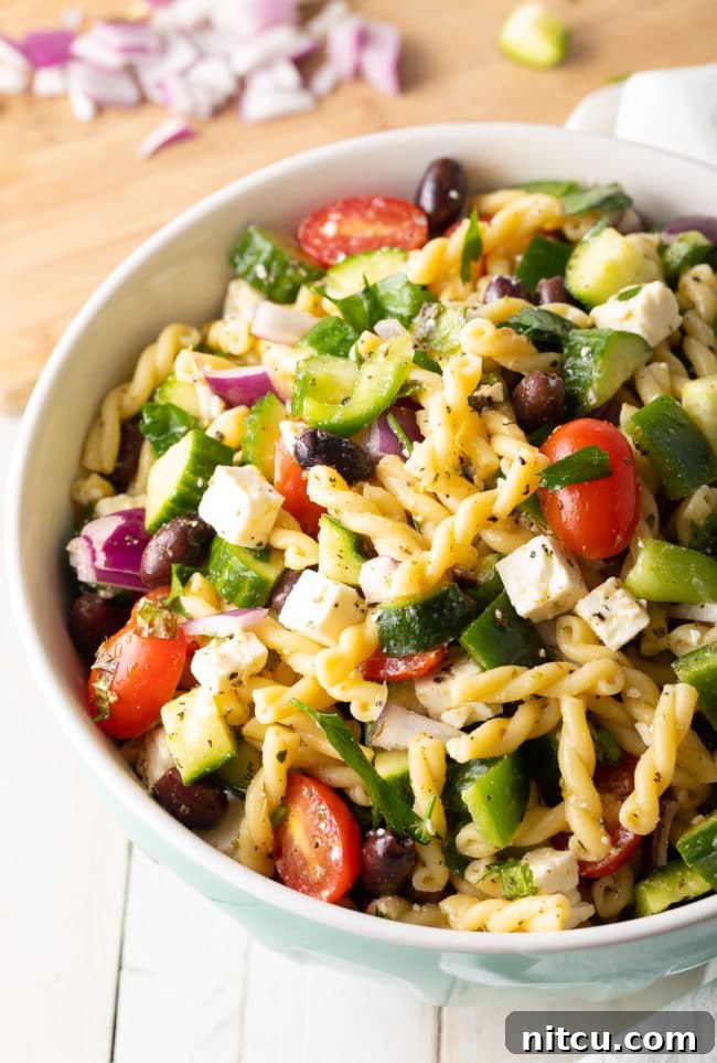 Easy Greek Pasta Salad mixed together with feta cheese, tomatoes, and cucumbers in a large serving bowl.