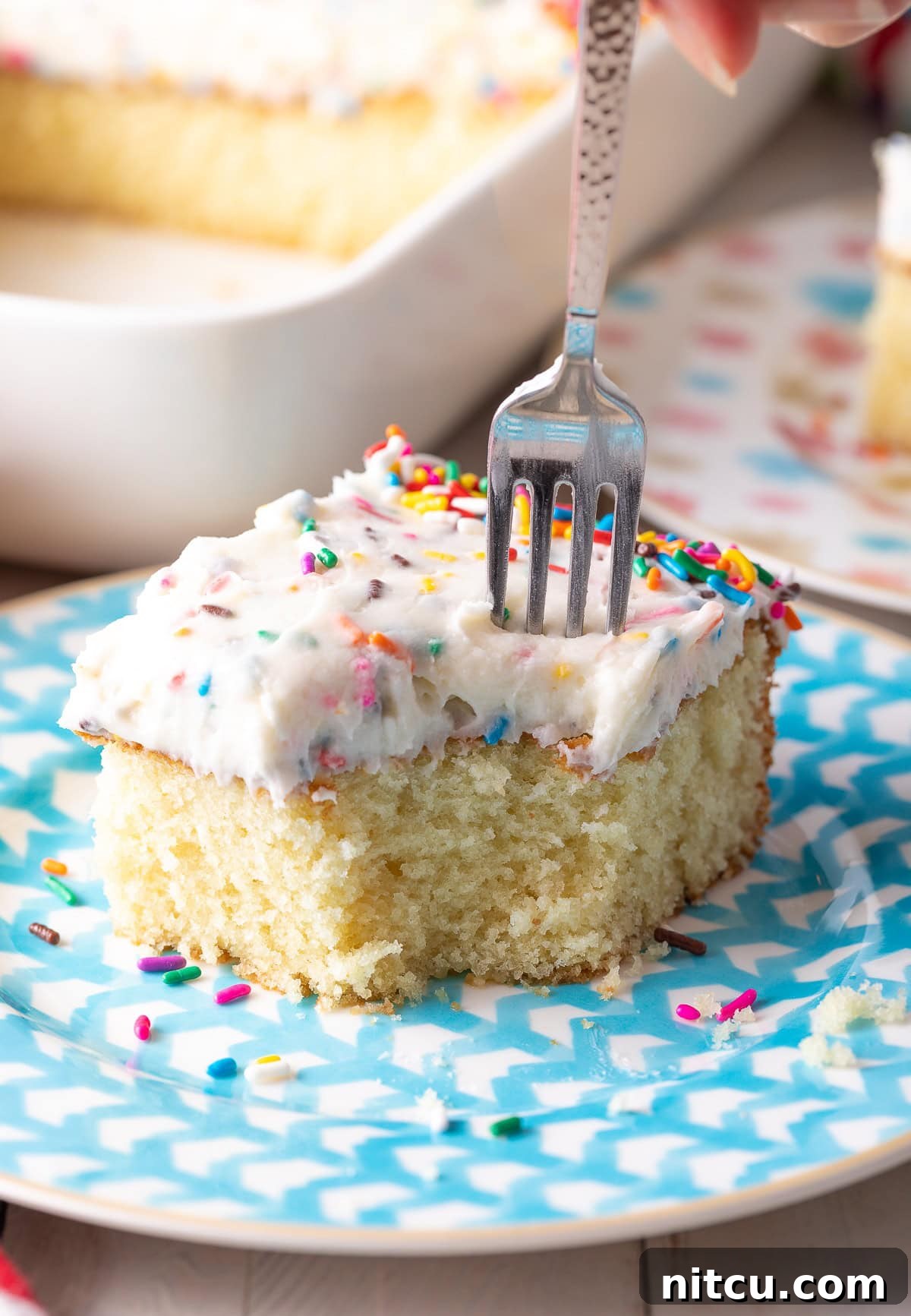 Fluffy Vanilla Cake From Scratch 12 A slice of vanilla cake on a plate with a fork poised to take a bite.