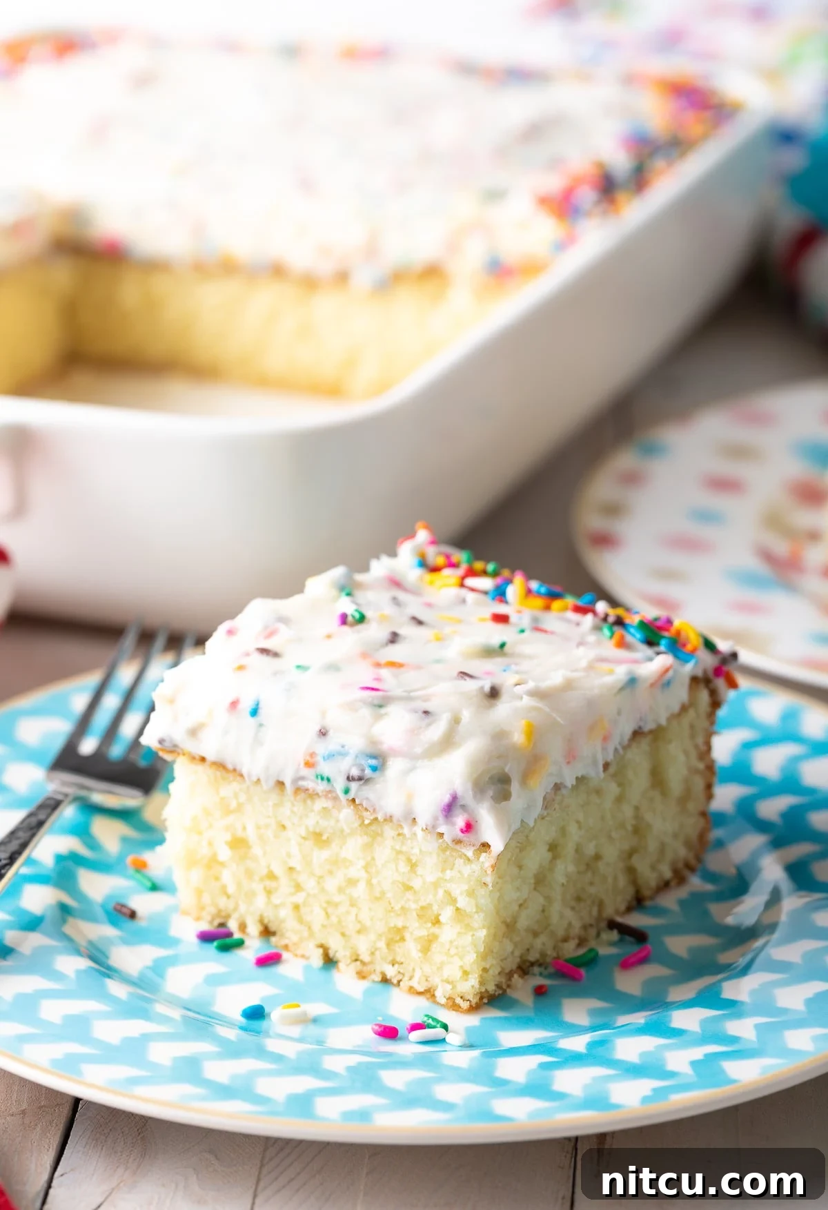 Fluffy Vanilla Cake From Scratch 5 A delectable slice of homemade vanilla cake adorned with vibrant funfetti frosting, elegantly presented on a blue plate.