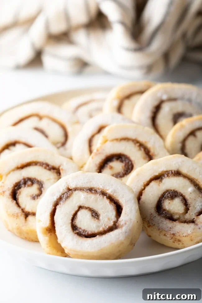 cinnamon-roll-cookies.jpg Close up of cinnamon roll cookies on plate, showing intricate swirls and delicate glaze