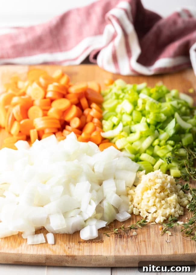 Nana's Masterpiece Chicken and Rice 6 Chopped white onion, carrots, celery and garlic on a cutting board, prepared for cooking chicken and rice.