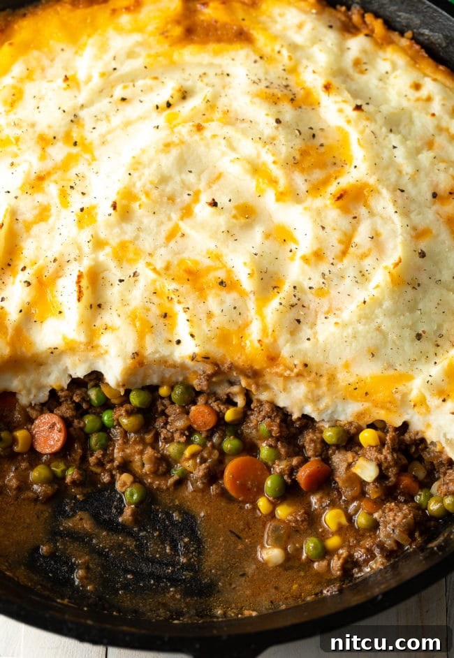 A delicious Cottage Pie with a scoop taken out, revealing the hearty beef and vegetable filling beneath a golden mashed potato crust.