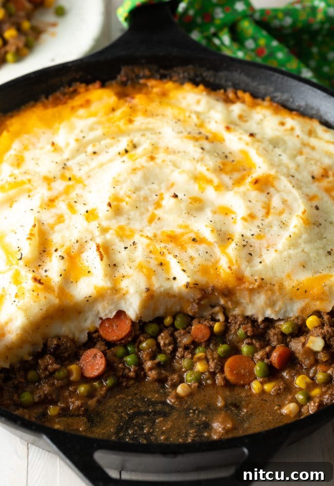 A close-up view of the Cottage Pie in a cast iron skillet, with a section scooped out to show the rich beef and vegetable filling.