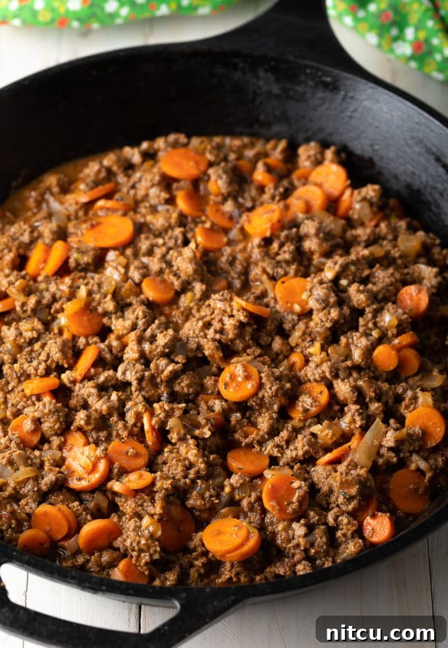 Sautéing ground beef with chopped onions and carrots in a cast iron skillet.