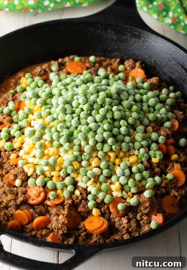 The beef and vegetable filling simmering in a cast iron skillet, with corn and peas mixed in.