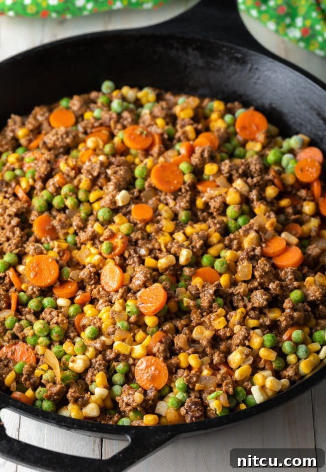The beef and vegetable filling spread evenly across the bottom of a cast iron skillet, ready for the mashed potato topping.
