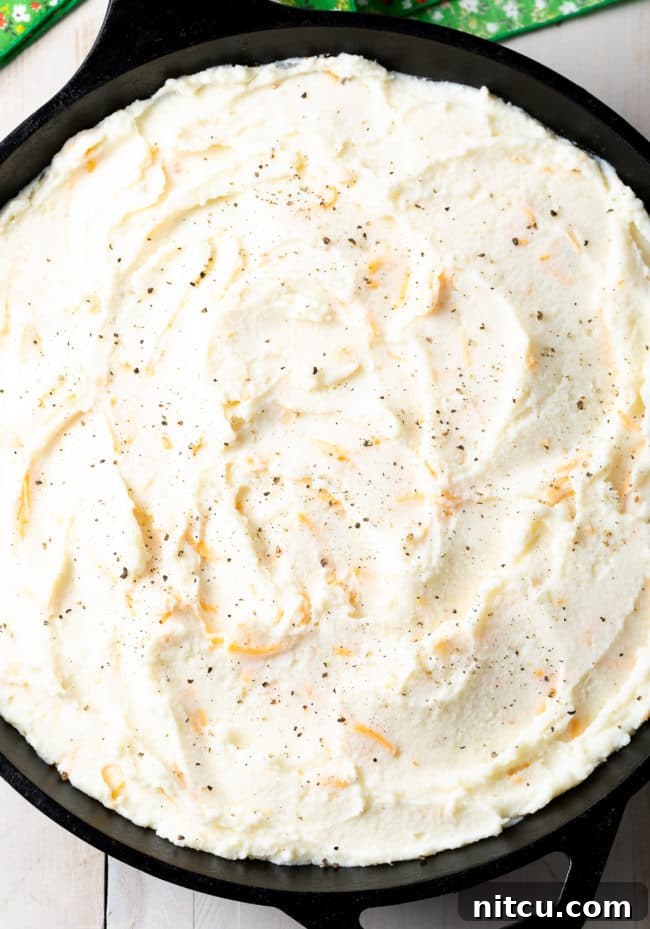 An assembled Cottage Pie in a cast iron skillet, topped with an even layer of mashed potatoes, ready for the oven.