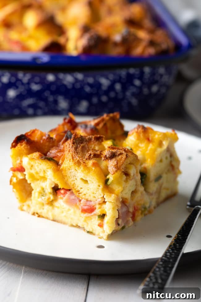The Ultimate Make-Ahead Breakfast Strata 3 egg strata - cut on plate with fillings poking out of fluffy layers
