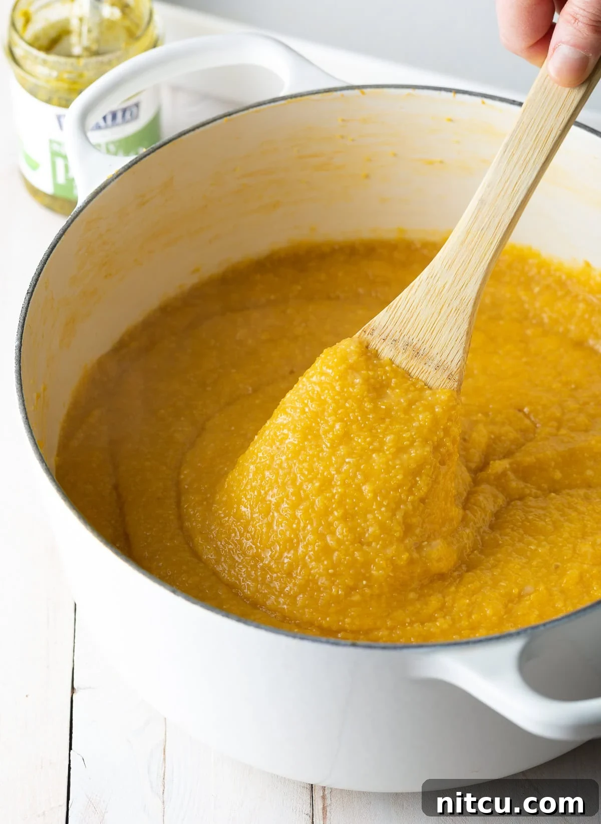 Golden Polenta Bake 5 Cooked polenta simmering in a pot, being gently stirred with a wooden spoon to achieve a smooth and creamy texture.