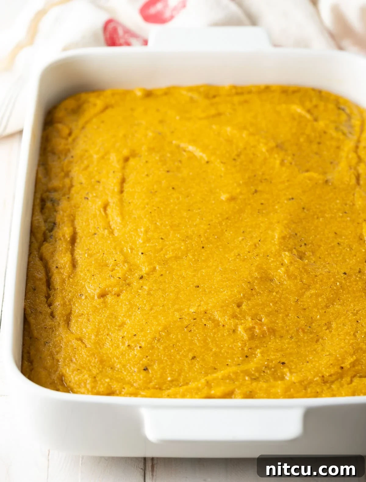 Golden Polenta Bake 6 A thick, even layer of prepared polenta, infused with cheese and pesto, freshly poured into a baking dish, ready for its initial bake.