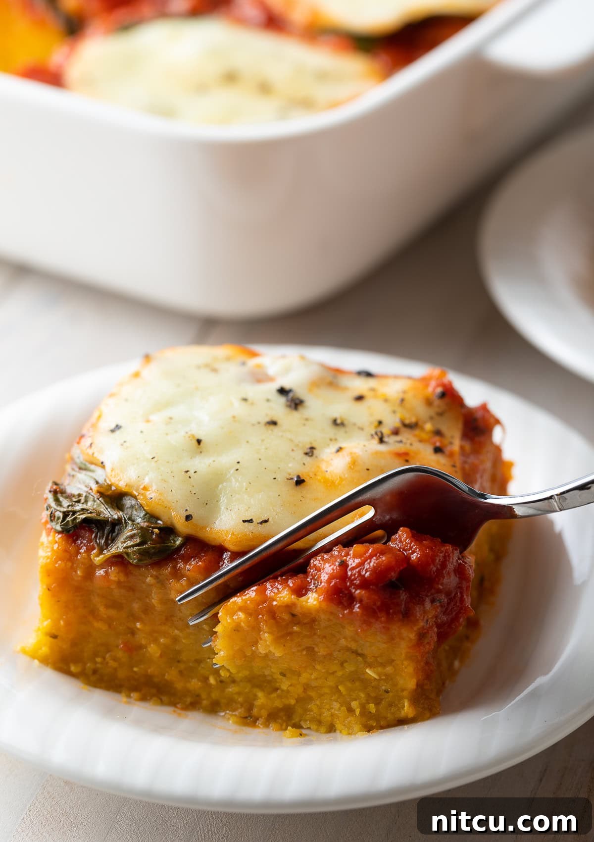 Golden Polenta Bake 9 A fork lifts a perfectly cut chunk of cheesy baked polenta from a plate, showing its inviting layers.