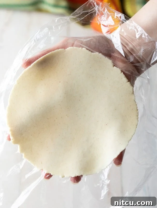 A delicate, uncooked corn tortilla, expertly peeled off the plastic sheet, ready for cooking on the comal.