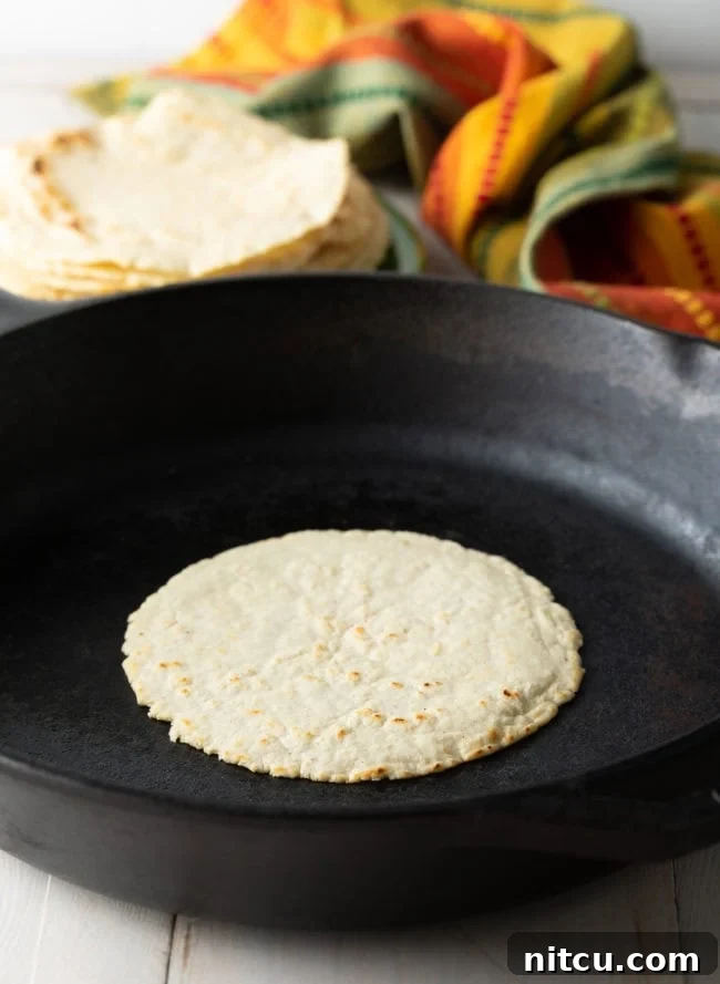 A corn tortilla cooking on a hot cast iron skillet, showing a slight puff and golden brown spots developing.
