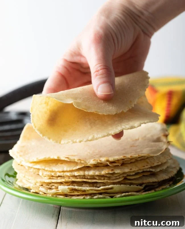 A hand gently folding a freshly cooked, perfectly soft corn tortilla, highlighting its excellent pliability and tender texture.