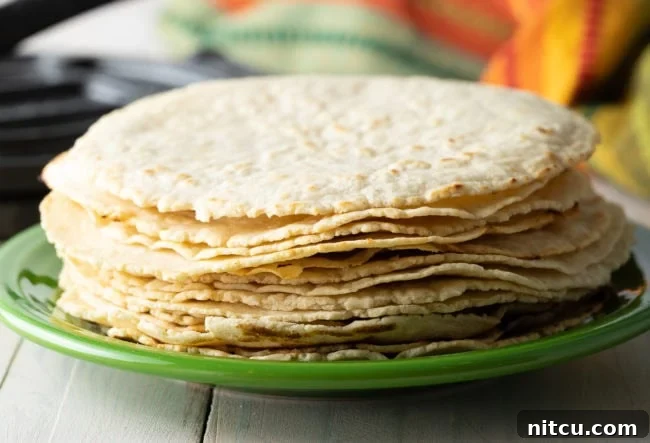A neatly stacked pile of golden, warm homemade corn tortillas rests on a ceramic plate, ready for serving.