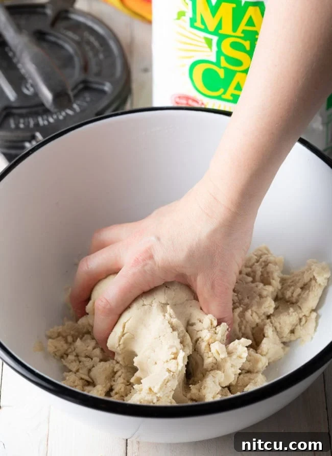 A hand expertly mixing the masa dough ingredients in a bowl until a smooth and consistent texture is achieved.