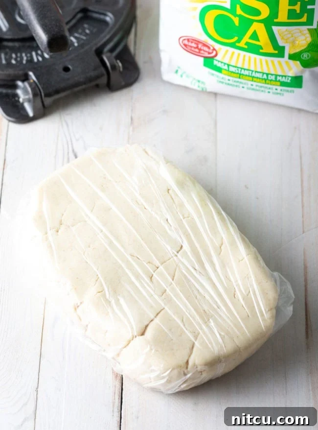 A rectangle of masa dough securely wrapped in plastic wrap, resting on a counter to ensure optimal hydration and pliability.