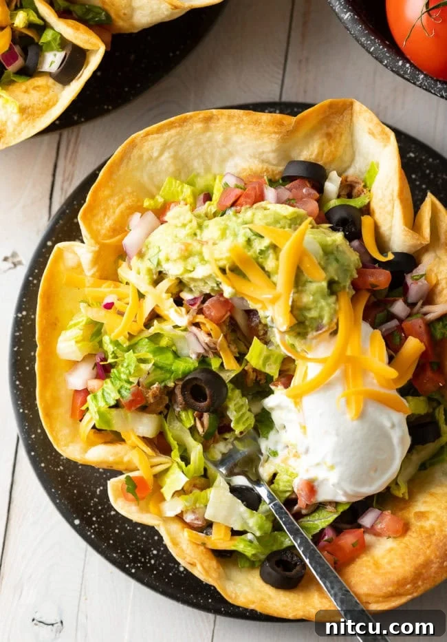 A perfectly crispy tortilla bowl, generously filled with a fresh taco salad, presented beautifully.