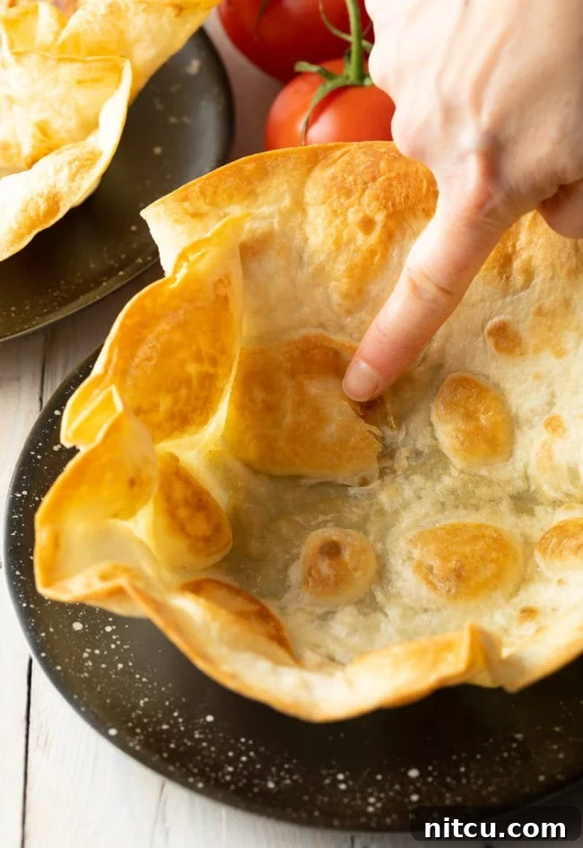 A hand gently tapping a crispy, homemade tortilla bowl on a plate to demonstrate its crispness.