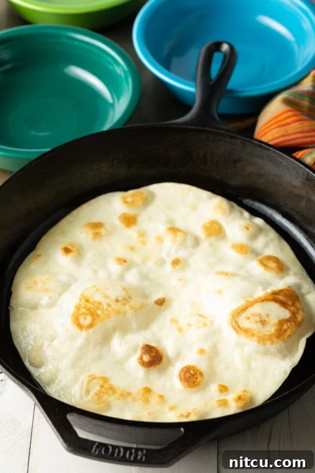 A flour tortilla sizzling in a pan with oil, beginning to form bubbles.