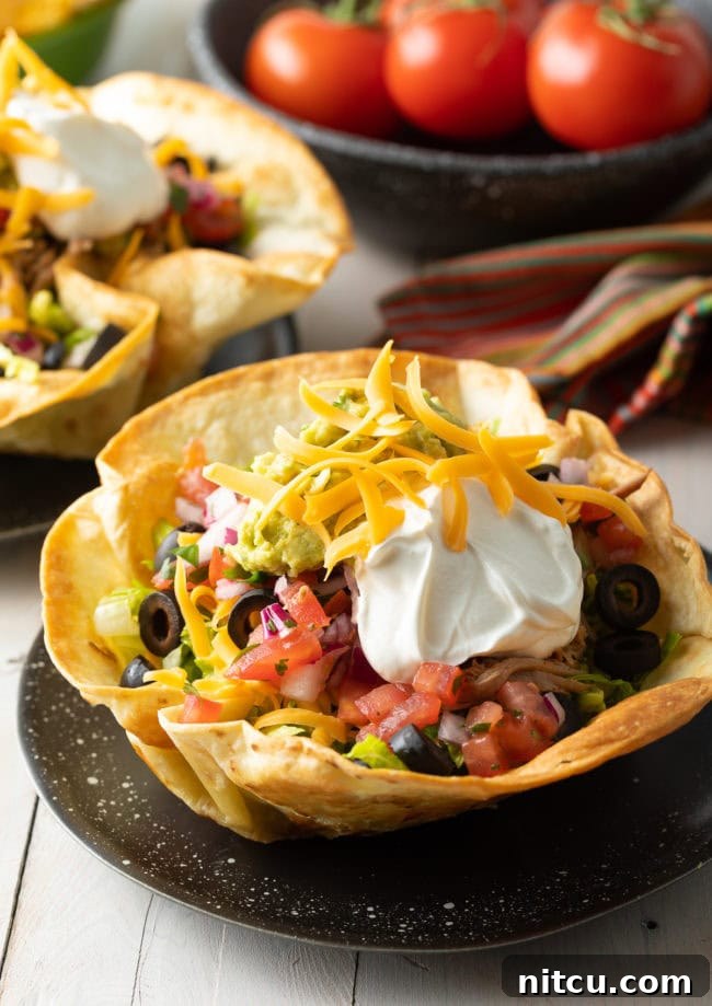 Two crispy tortilla bowls, generously filled with colorful taco salad ingredients, served on elegant black plates.